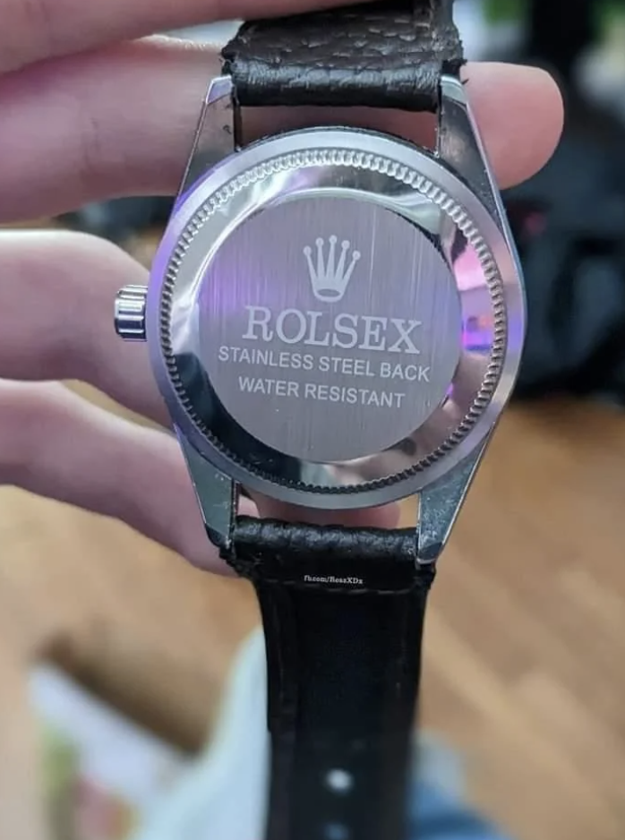 A close-up of the back of a wristwatch labeled &quot;ROLSEX STAINLESS STEEL BACK WATER RESISTANT.&quot; It appears to be a knock-off of a Rolex watch