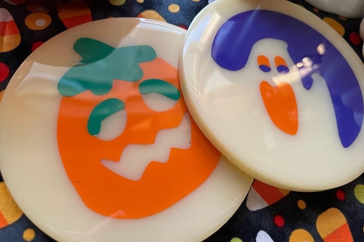 Close-up of two cookie shaped Halloween coasters: one with a pumpkin face and the other with a ghost face