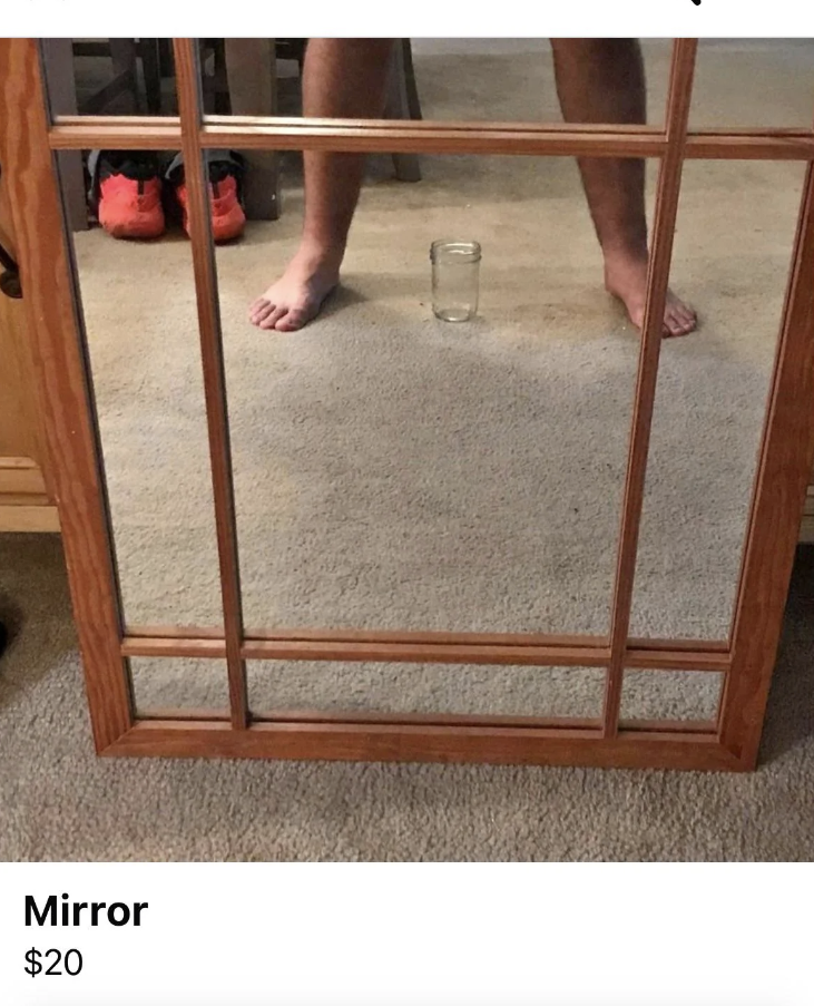 A mirror with a wooden frame is for sale at $20. In the reflection, bare feet and a glass of water on the carpeted floor are visible