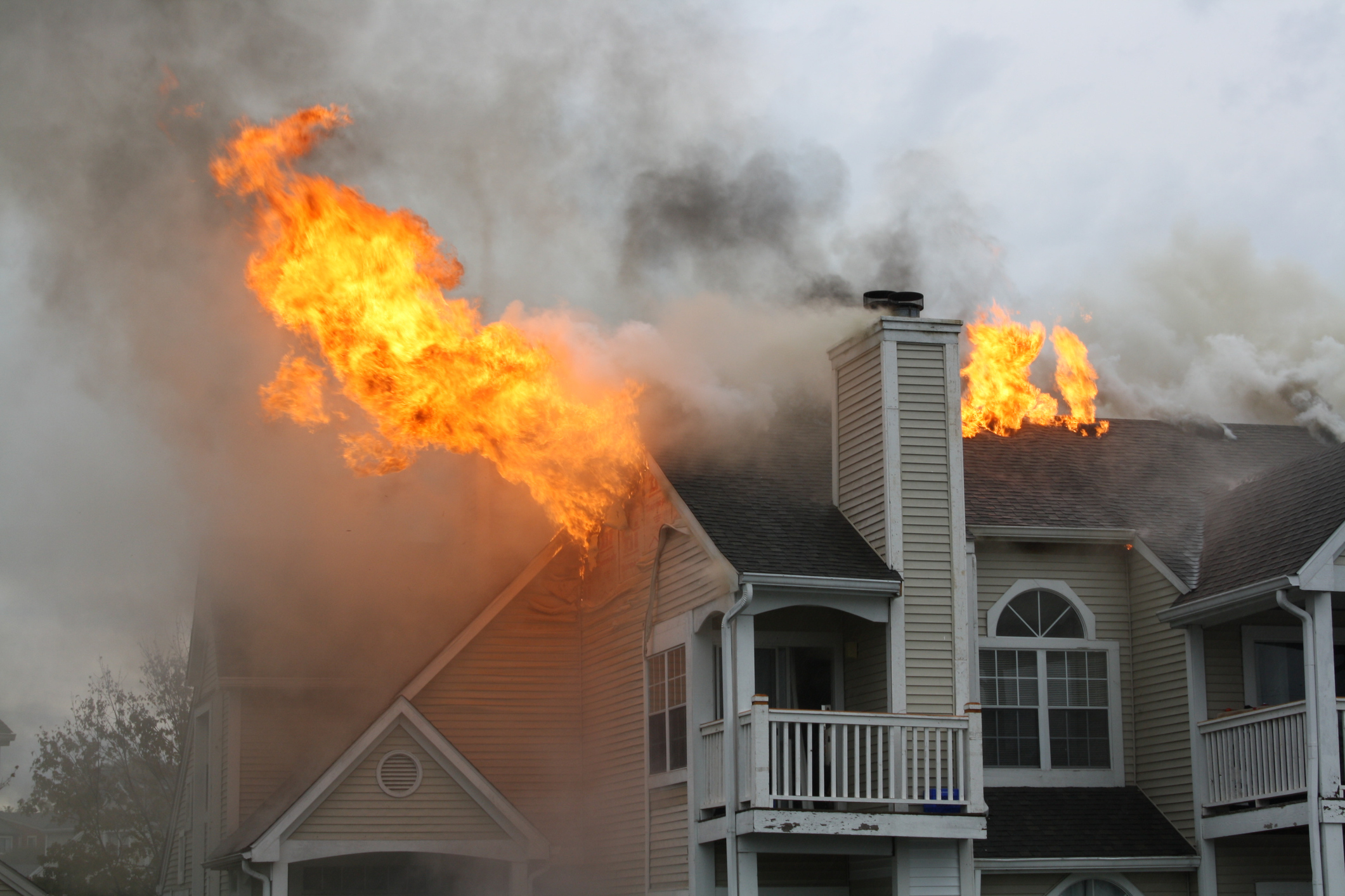 A house fire burns through the roof of a multi-story home with smoke filling the air