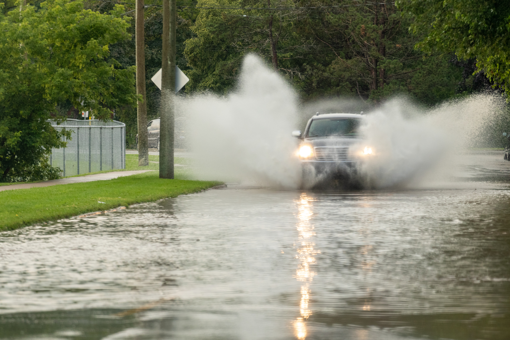 A car drives through a flooded street, causing large splashes of water