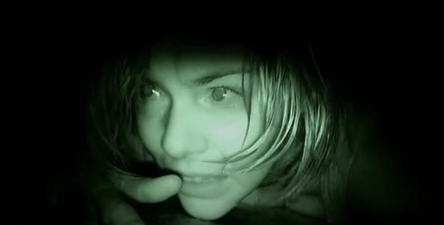 A close-up of a frightened woman with wet hair, dimly lit, appears to be in a dark, confined space. She looks up with wide eyes