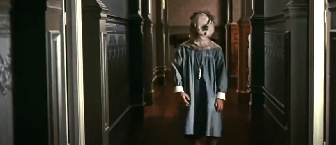 Child in a hallway wearing a creepy mask and old-fashioned clothing