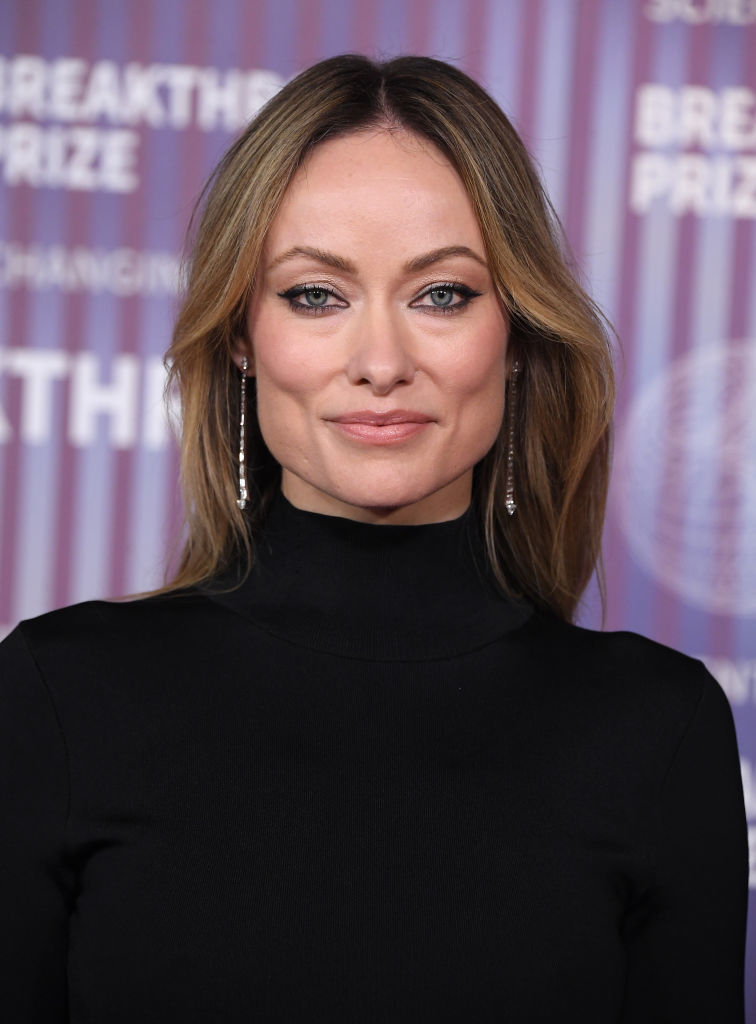 Olivia Wilde is on the red carpet wearing a sleek black outfit with long earrings at the Breakthrough Prize event