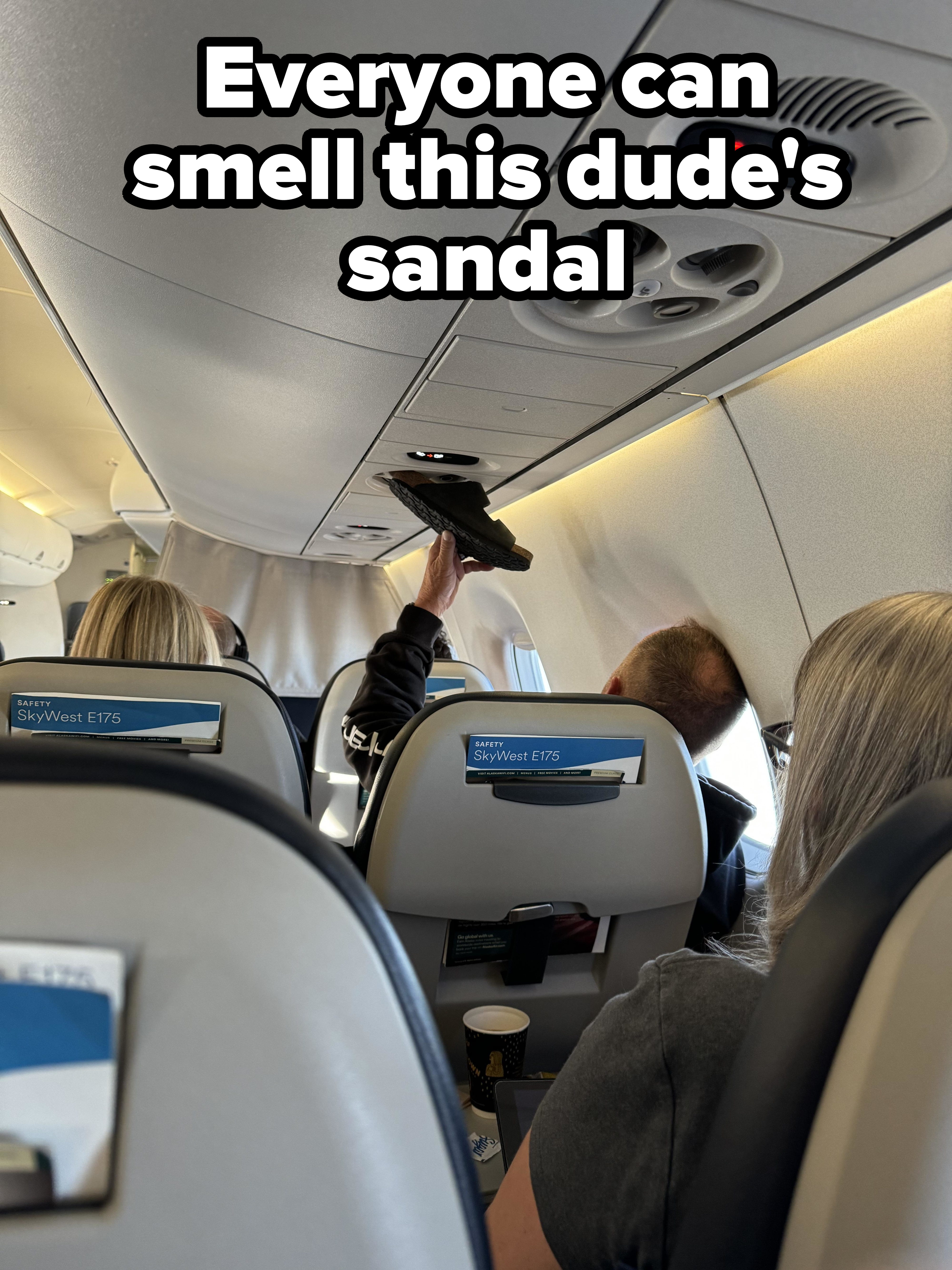 Passengers seated inside an airplane with one person adjusting the overhead compartment. SkyWest E175 airline seats are labeled in the image