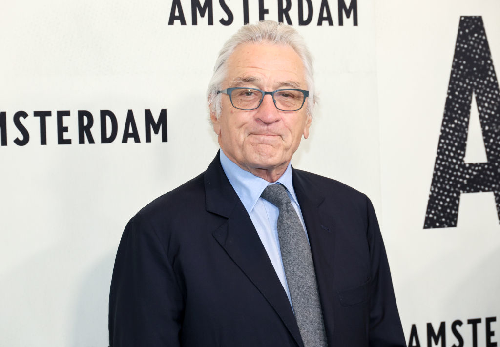 Robert De Niro at a premiere event for &quot;Amsterdam&quot; wearing a formal dark suit, light dress shirt, and tie, standing in front of a backdrop with the film&#x27;s title