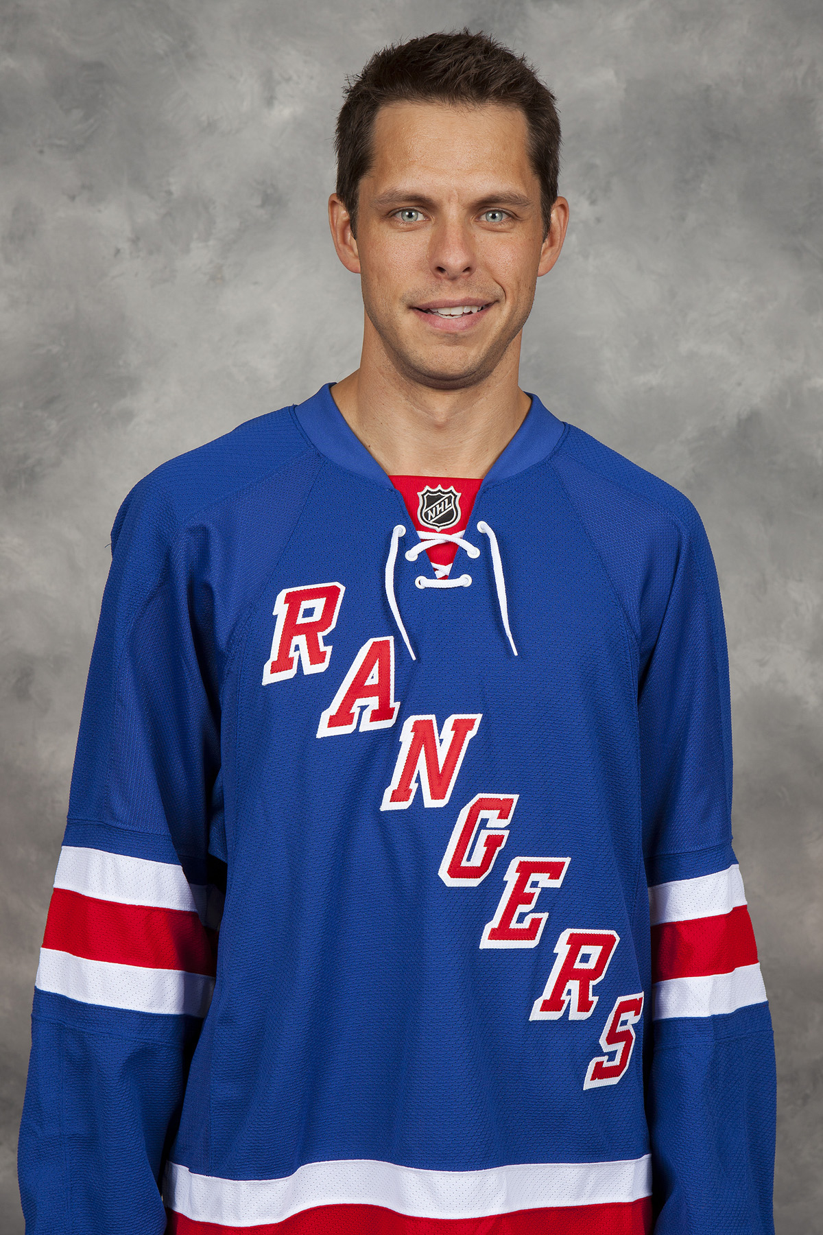 A person standing and smiling, wearing a blue New York Rangers hockey jersey with red and white stripes