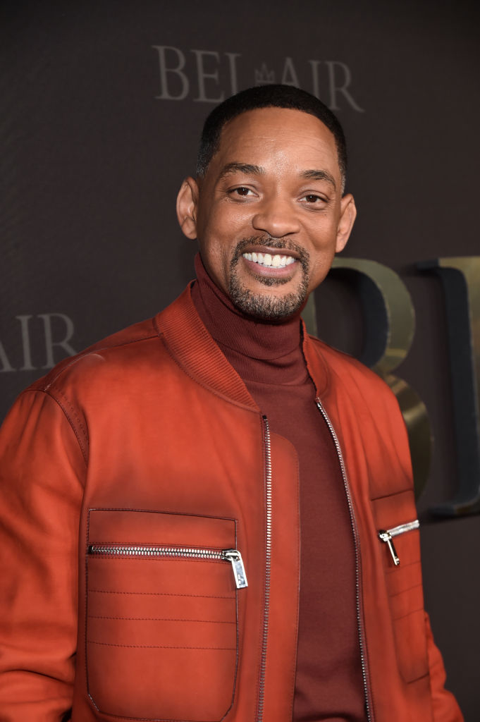 Will Smith smiling, wearing a red jacket with zipper pockets over a matching red turtleneck, at a &quot;Bel-Air&quot; event