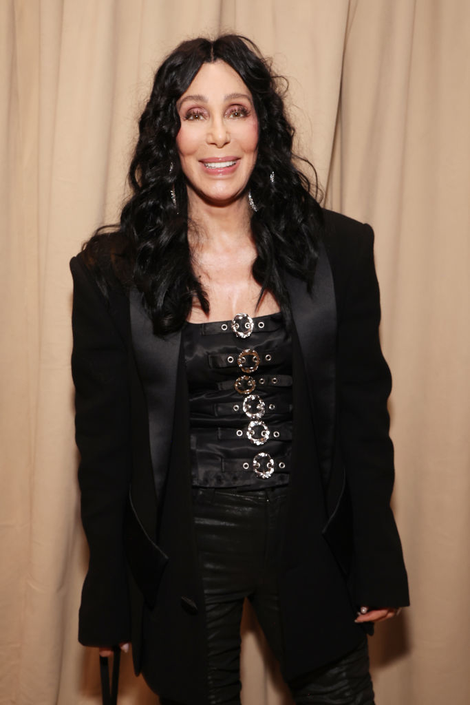 Cher in a stylish black ensemble featuring a corset and blazer, smiling at an event