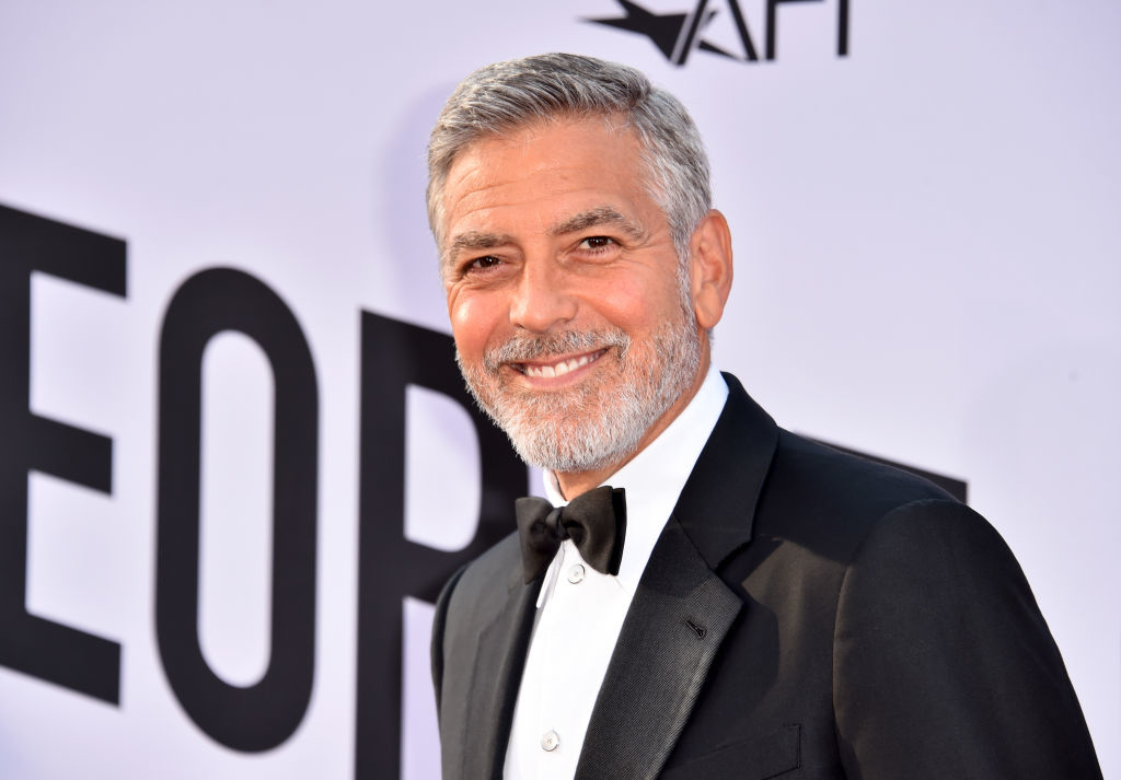 George Clooney in a black tuxedo, smiling on the red carpet at an event