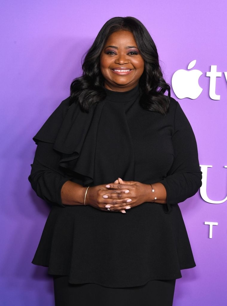 Octavia Spencer poses in an elegant black outfit on a carpet with an Apple TV+ backdrop