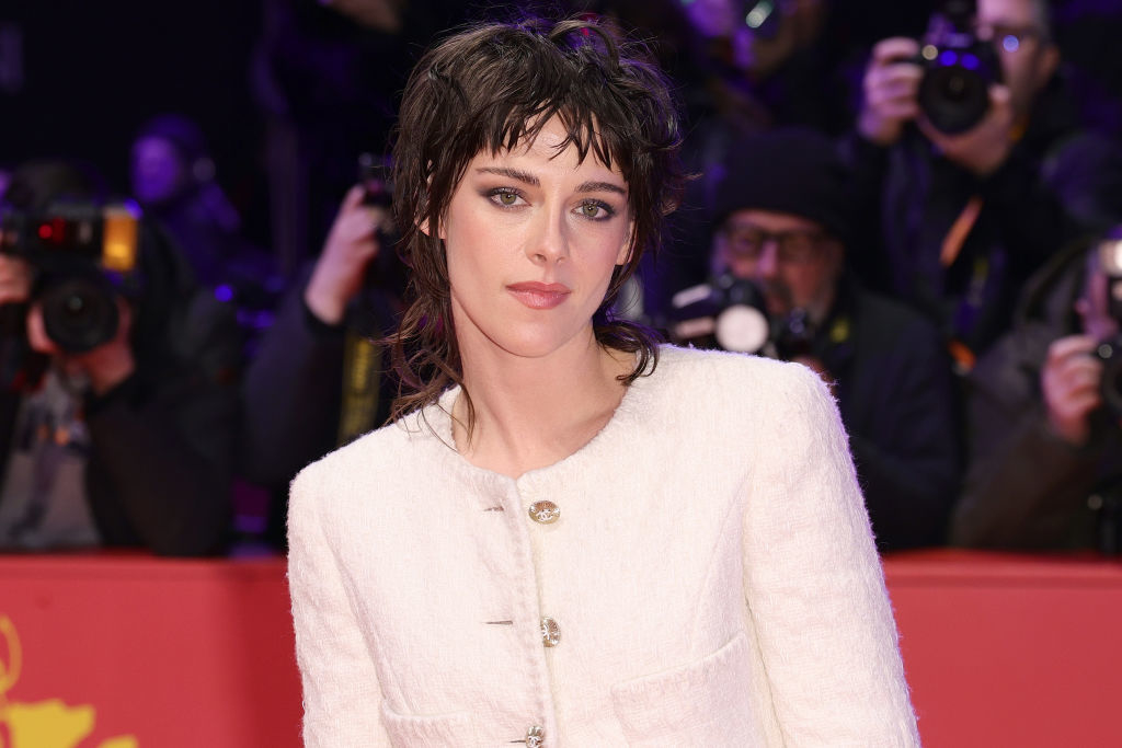 Kristen Stewart poses in a chic outfit at a red carpet event, with photographers in the background