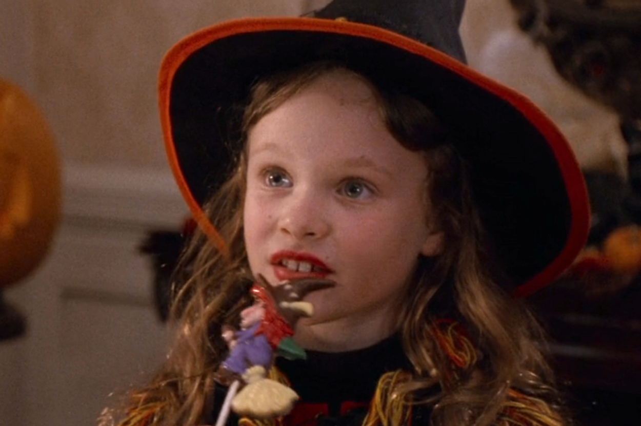 Dani from Hocus Pocus dressed as a witch, eating a lollipop