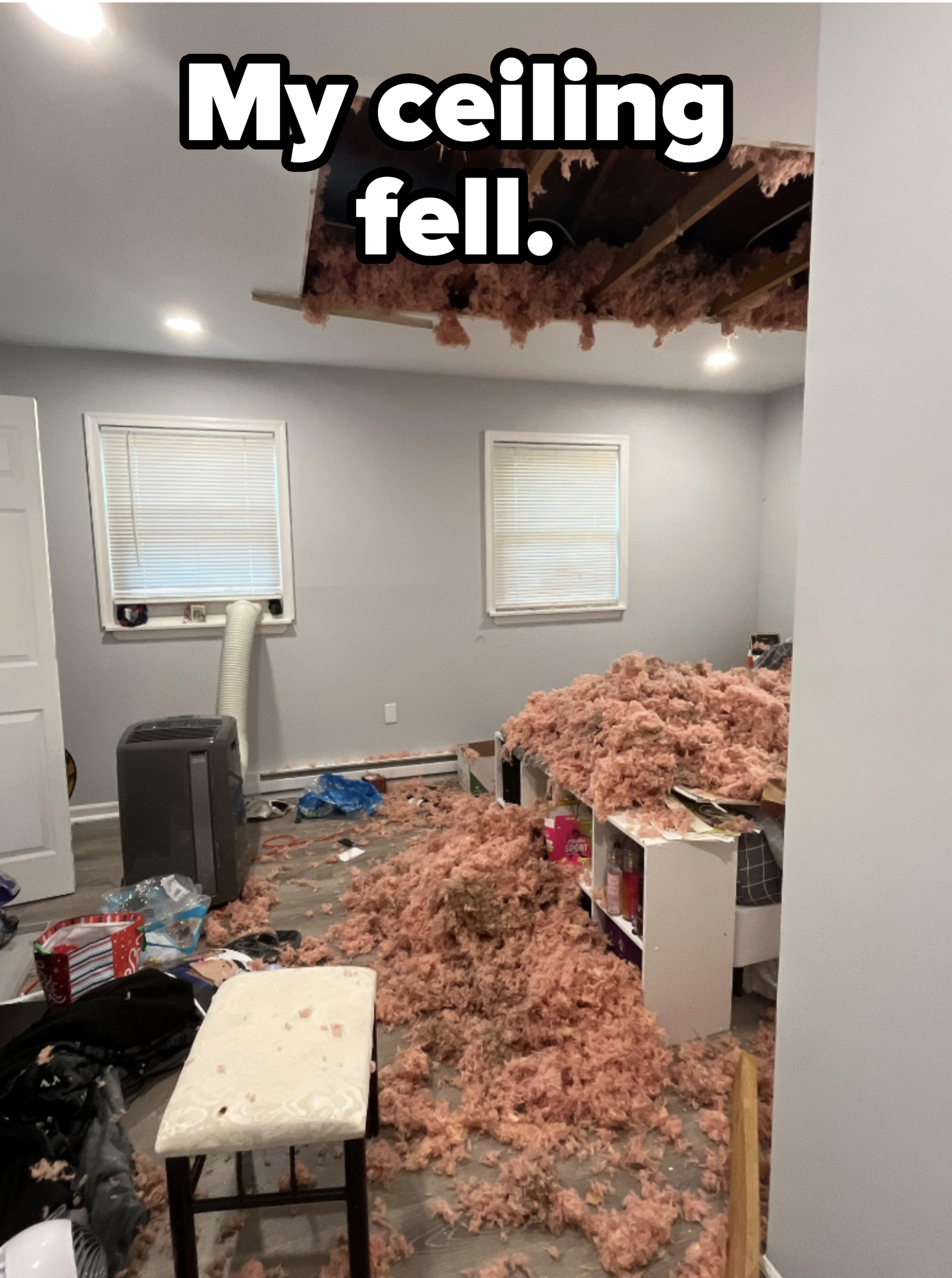 Room with large hole in the ceiling causing pink insulation to fall, covering the floor and furniture. Various items are scattered around the room