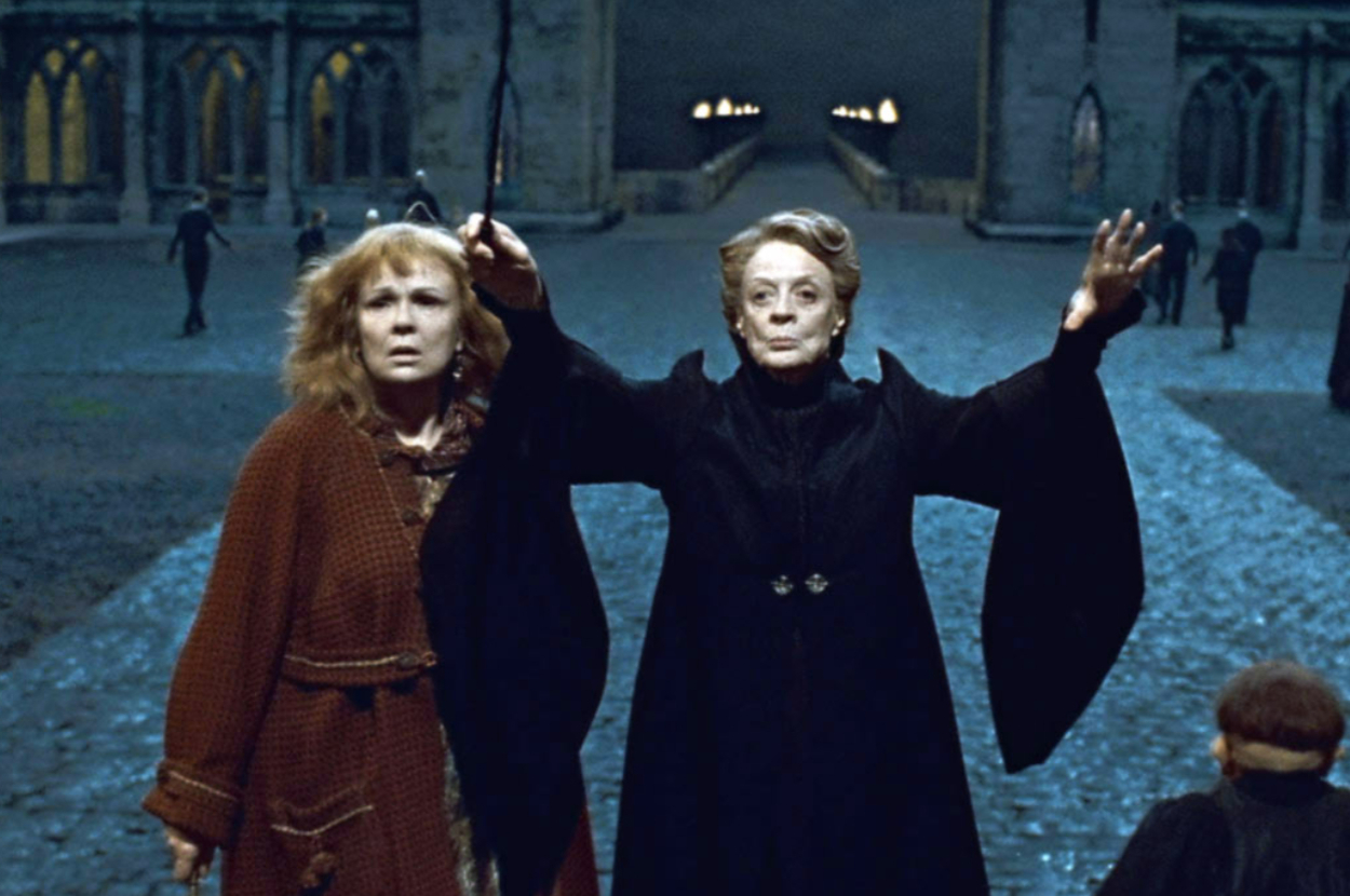 Julie Walters and Maggie Smith in dramatic attire, holding wands and casting spells outside a grand, mysterious building at night