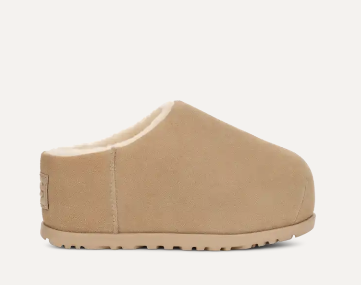 Tan suede slipper with a soft, rounded design and a fluffy interior. The sole is grooved for extra grip. A comfortable footwear option for indoor use