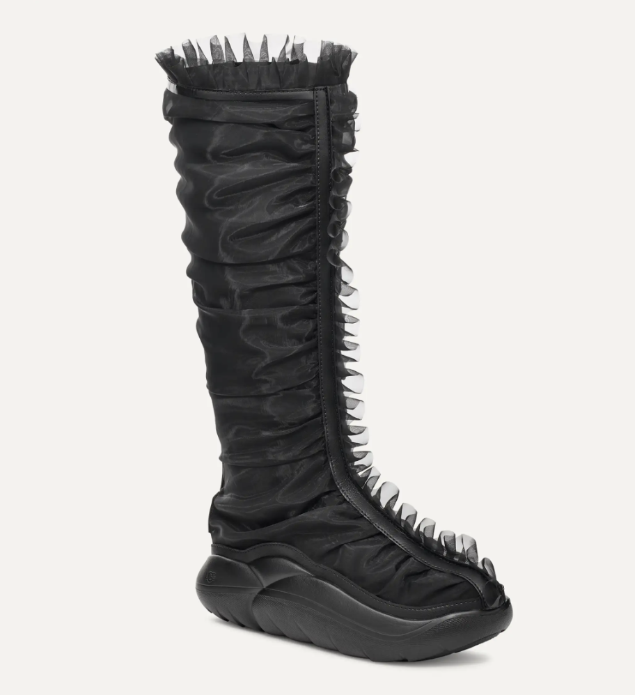 Knee-high boot with a ruched design, featuring a zipper and unique spiked detailing along the front. The sole is chunky with an angular shape