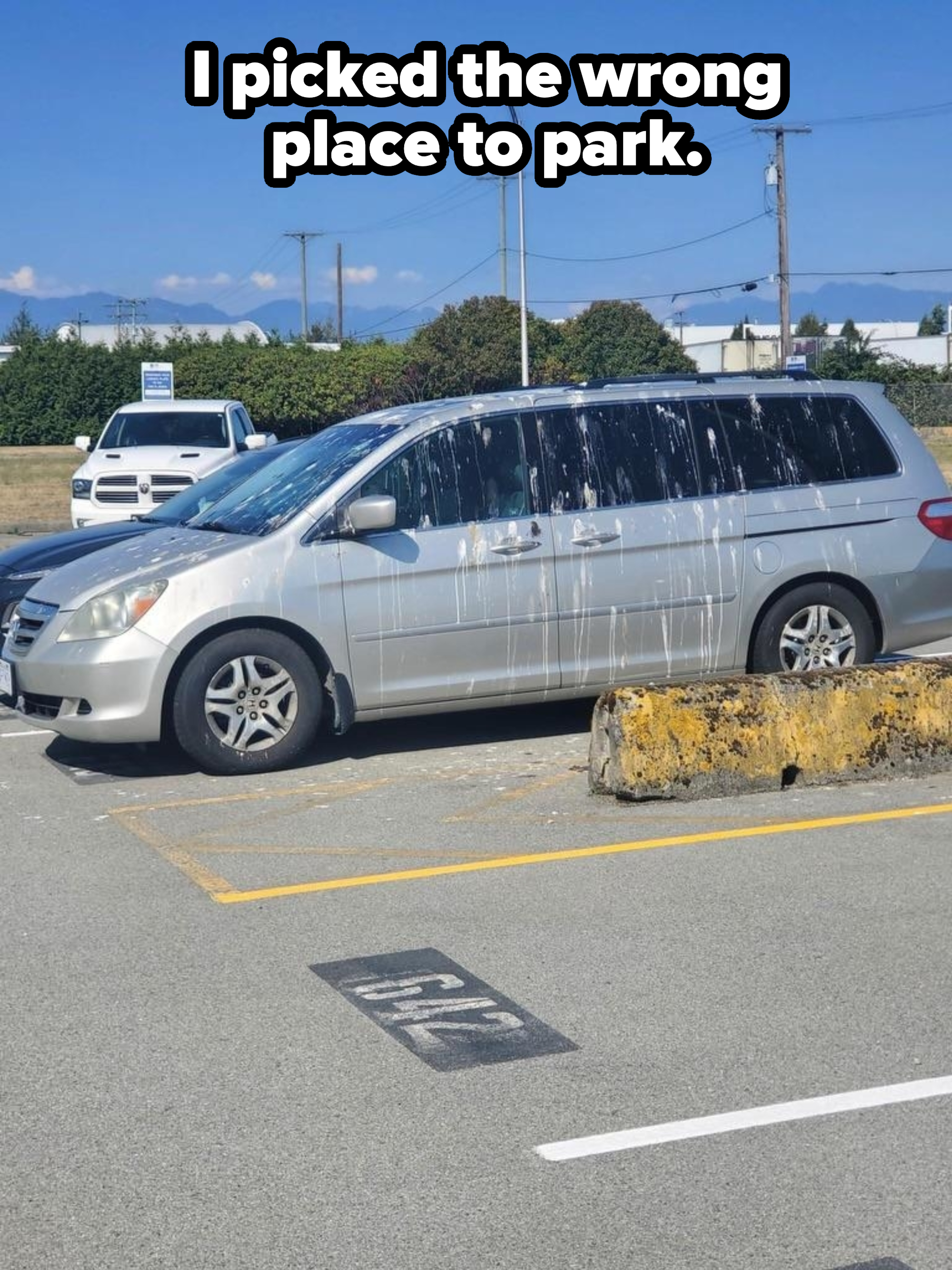 A silver minivan in a parking lot is splattered with a large quantity of white paint on its side and windows