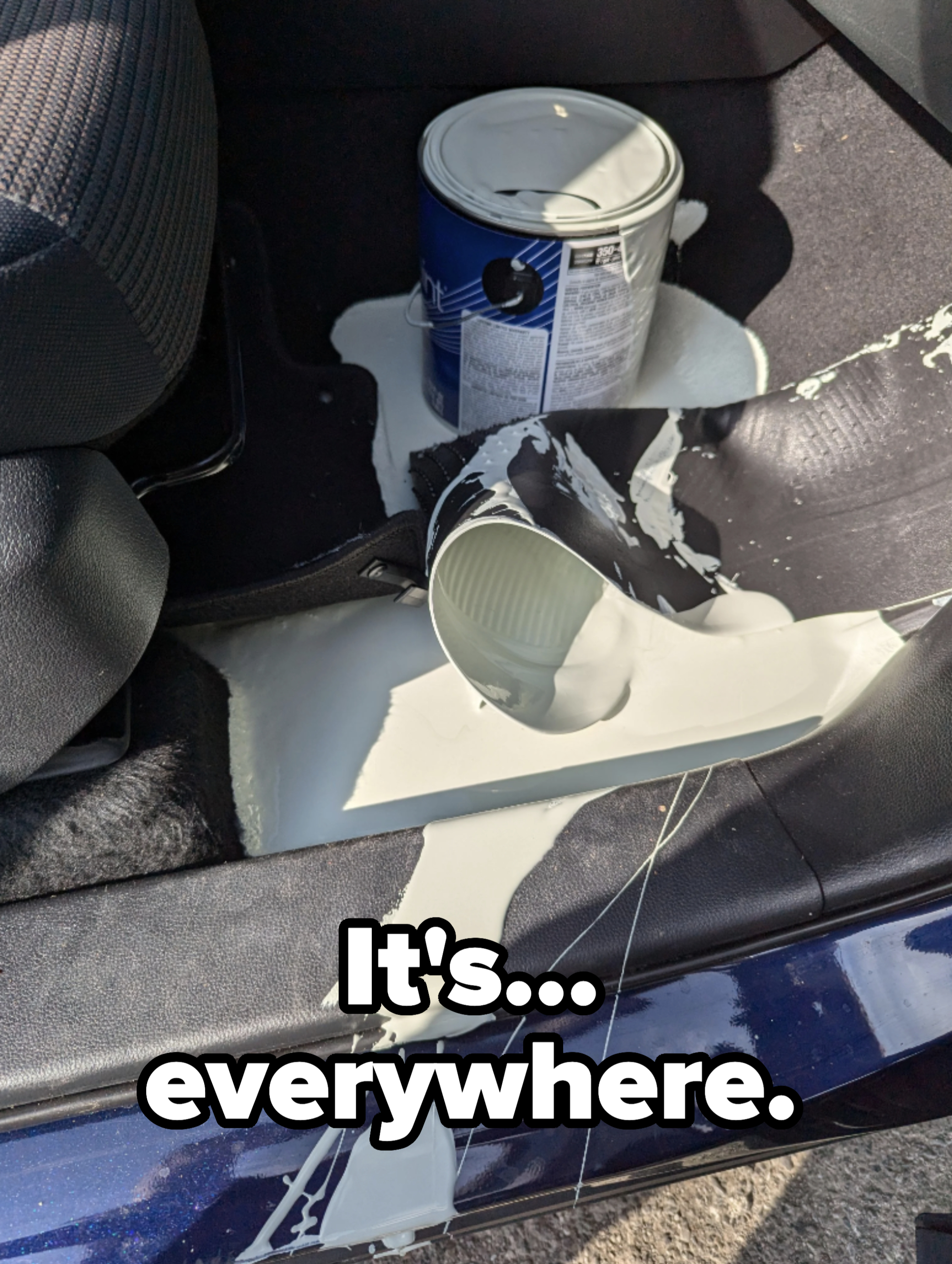 A spilled can of white paint on a car&#x27;s floor, with the paint spreading across the floor mat and into the car seat