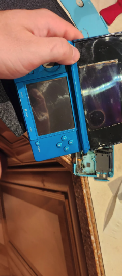 Close-up of a person&#x27;s hand holding a broken blue handheld gaming console with detached parts. No other text or people are in the image