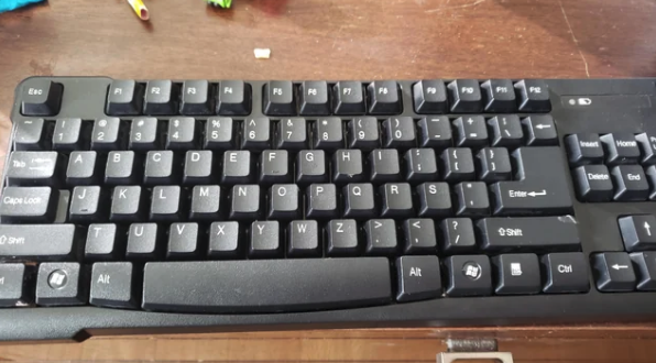 A black keyboard on a wooden surface with several keys and a portion of the desk visible