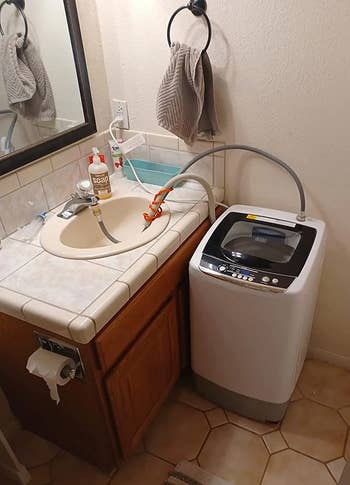 Portable washing machine connected to a bathroom sink with a flexible hose. A towel hangs by the mirror