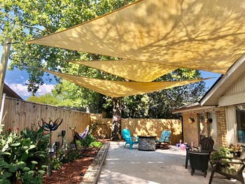 Backyard with three yellow triangle sunshades, seating area, plants, and decorative items, suggesting cozy outdoor living space essentials for shopping