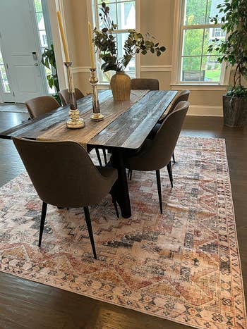 Wooden dining table with modern chairs on an ornate rug, set in a room with decor plants. Ideal for home furnishing inspiration