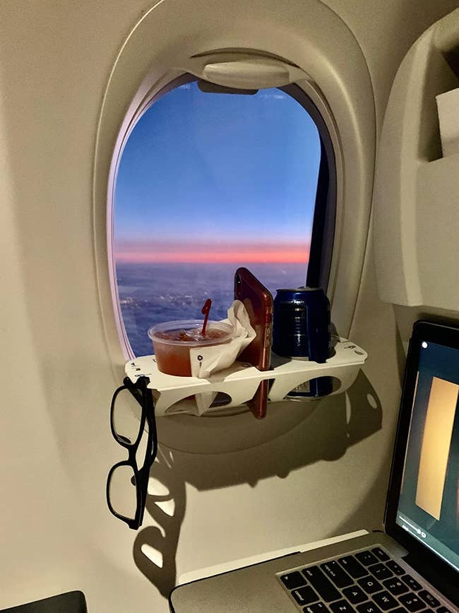 the tray attached to a window ledge holding two drinks, a phone, and a pair of glasses