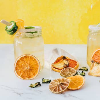 Jar of spicy margarita with garnish, surrounded by dried citrus slices, on a counter