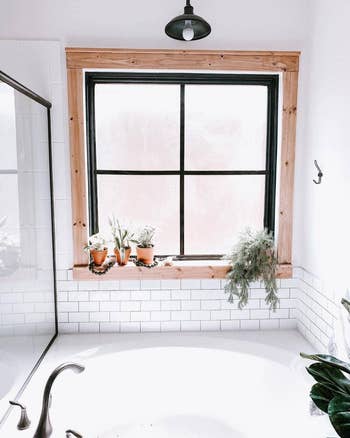 A bathroom window with plants on the sill, tiled walls, and a modern faucet