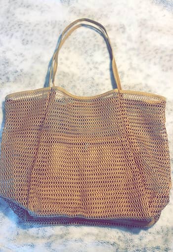 Woven beige tote bag with a simple, open-mesh design and two handles laid flat on a textured background