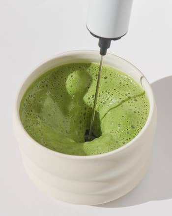 Electric frother mixing a creamy matcha tea in a ceramic cup