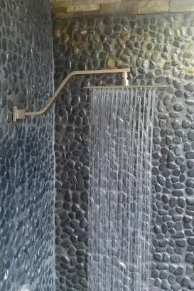 A wall-mounted showerhead with water flowing down in a bathroom with stone-textured walls