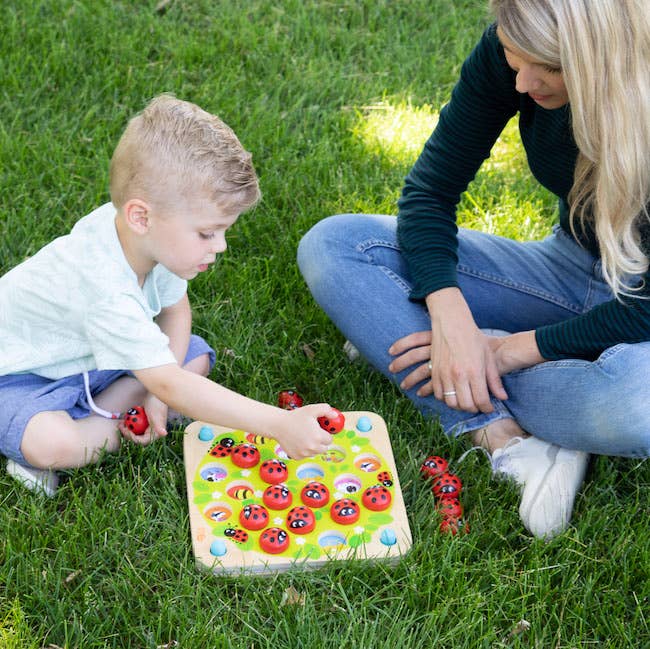 A child and an adult play with a ladybug-themed toy on the grass
