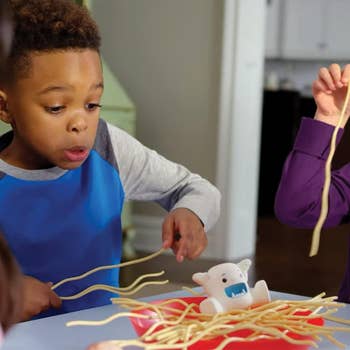 Children playing with noodles around a Yeti toy at a kitchen table