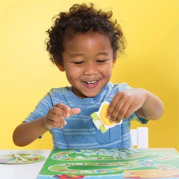 A child in a blue shirt smiles while playing a colorful board game with a yellow background