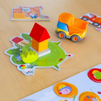 Kid's toy set with a small toy house on a puzzle mat, a toy truck, and puzzle pieces with illustrated animals and objects