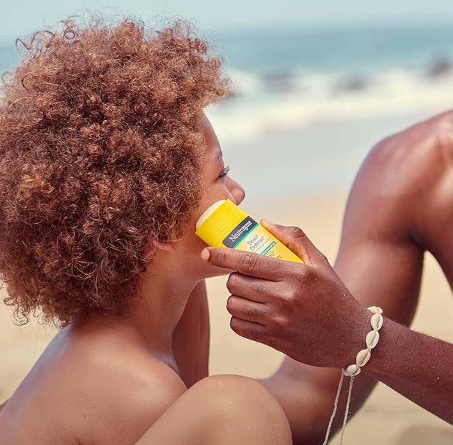 a model applying the sunscreen stick to a child's face