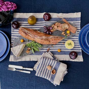 Flat lay of a rustic bread loaf, cheese, fruits, nuts, and cutlery on a striped cloth