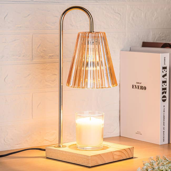 Table lamp with a pleated shade and wooden base next to a candle and book, providing warm lighting