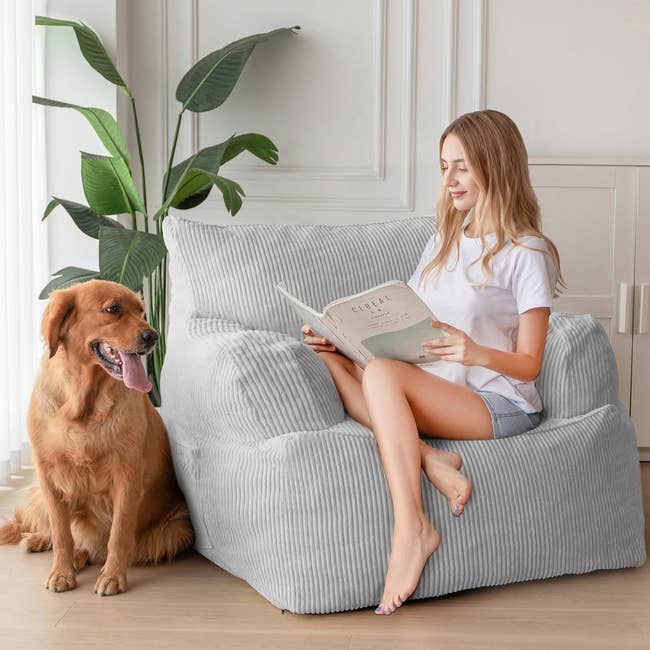 Woman sitting on a bean bag chair reading a book next to a Golden Retriever