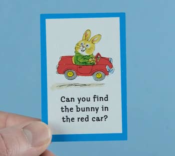 A hand holds a card with a drawing of a bunny riding in a red car and the text 