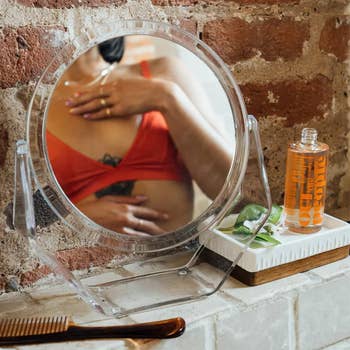 Reflection of a person in a mirror with a skincare product beside them, indicating a beauty and self-care setting