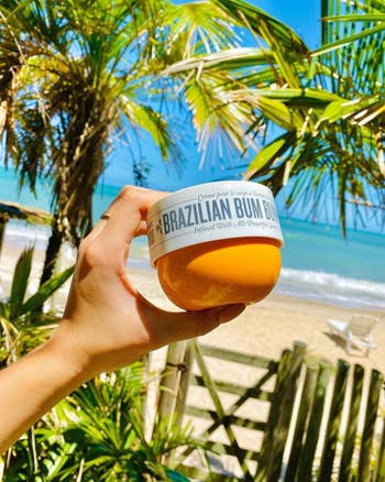 model holding a jar of Brazilian Bum Bum Cream in a tropical beach setting 