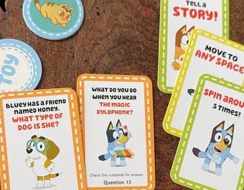 Various Bluey-themed game cards are spread out on a table, featuring questions and instructions for players