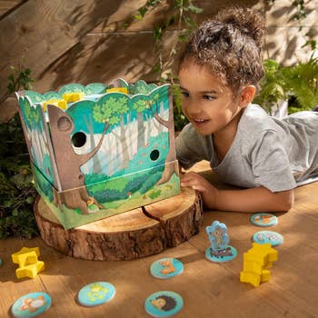 Young child plays with a forest-themed DIY toy box surrounded by nature-inspired game pieces. Perfect for imaginative playtime shopping