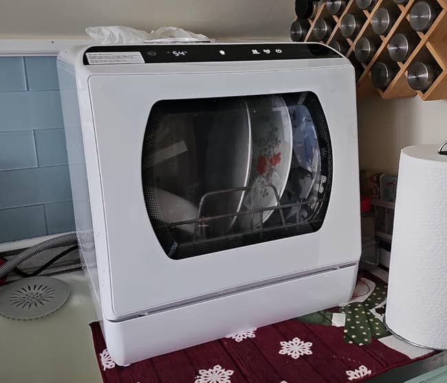 A countertop dishwasher filled with dishes, beside a wine rack and paper towels