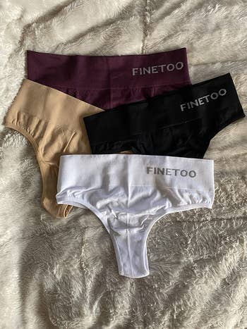 reviewer photo of four of the thongs spread out on a bed, with Finetoo logo printed on them