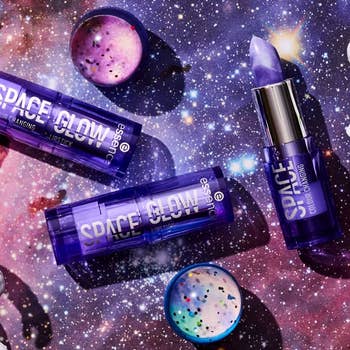 Essence Space Glow color-changing lipsticks and lip glosses with space-themed packaging arranged on a galaxy-patterned background